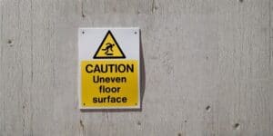 Caution sign warning of uneven floor surface at Pinnacle Structural Repairs.